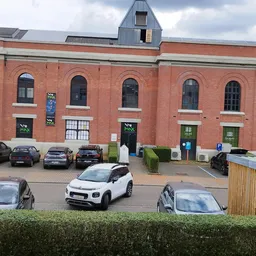 Bakstenen gevel van kringloopwinkel met groene deuren, parkeerplaats met auto's voor het pand