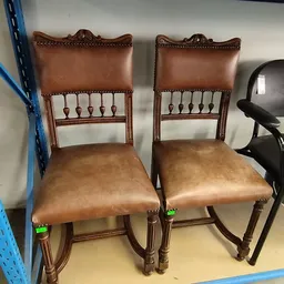 Twee bruinleren stoelen met houten frame en decoratieve nagelingen op de zitting
