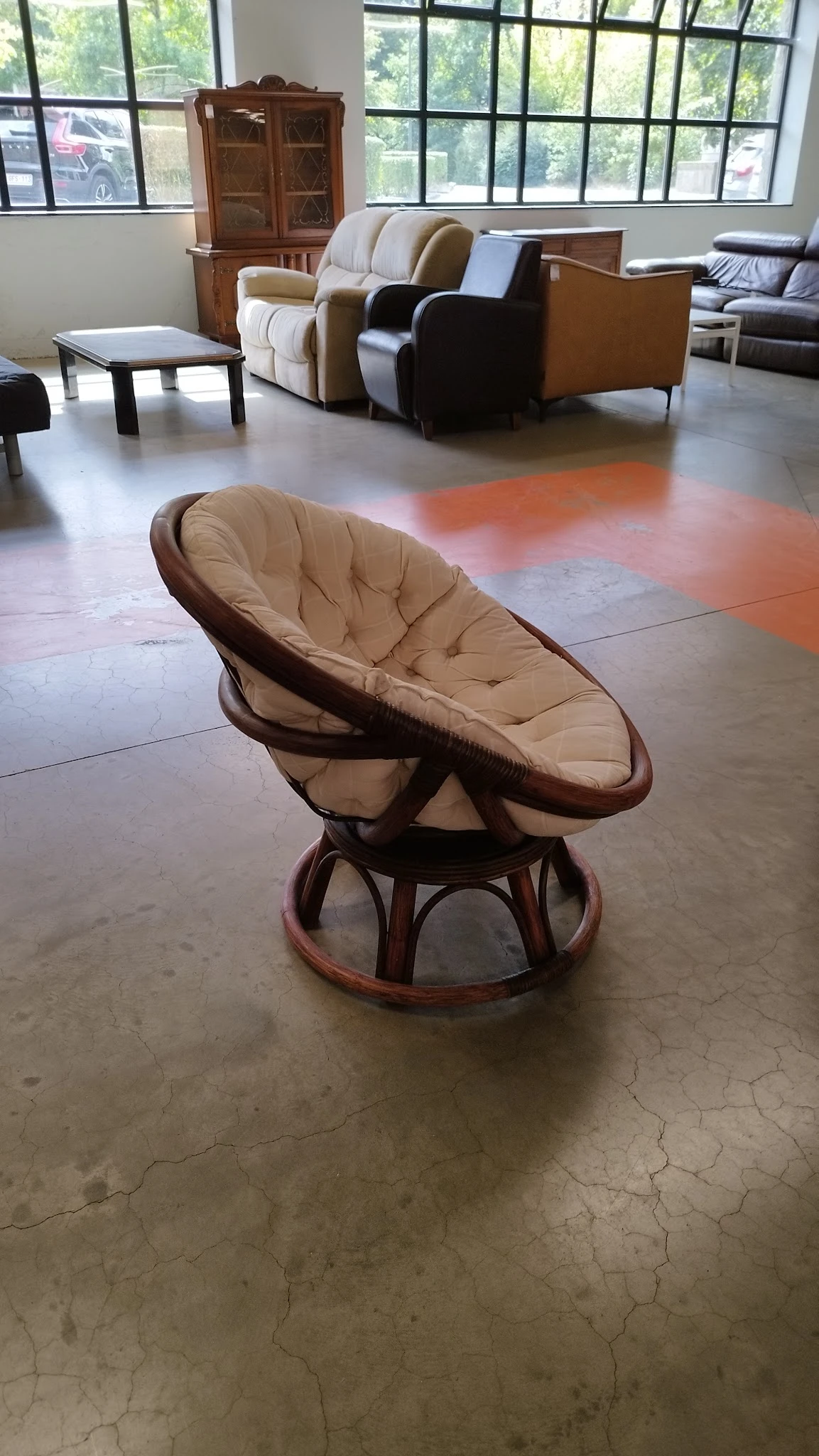 Bruine rotan schommelstoel met beige kussen op tegelvloer