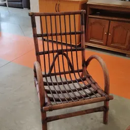 Houten fauteuil met rieten/rotan zitting en rugleuning, bruin gekleurd, staand in een kringloopwinkel