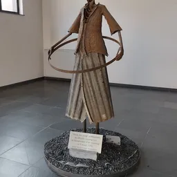 Bronzen beeldhouwwerk van een figuur met uitgestrekte armen op een stenen sokkel met naamplaatje