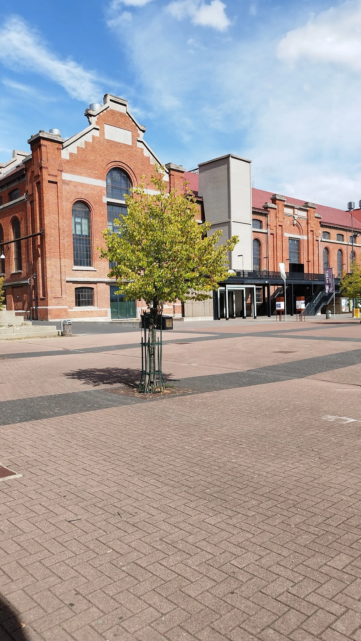 Marktplein met bakstenen gebouwen, jong boompje en zwart paviljoen