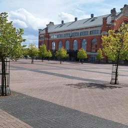 Rood bakstenen gebouw met grote ramen aan een plein met tegels en jonge bomen