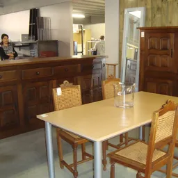 Winkelbinnenruimte met eettafel en stoelen, houten meubels op de achtergrond en balie met personeel