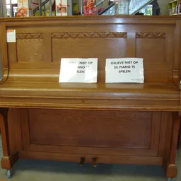 Bruine houten piano met waarschuwingsbriefjes 'niet op de piano spelen' op de klep