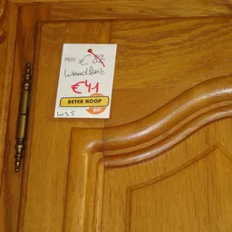 Houten meubeldeel met golvende carving en prijssticker, naast een penseel op houten ondergrond