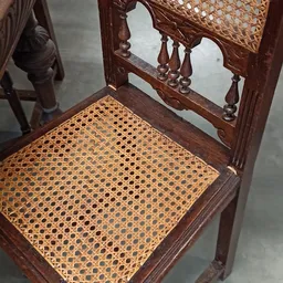 Close-up van een houten stoel met gevlochten rotan zitting en gesneden rugleuning