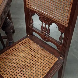 Gedetailleerde close-up van een antieke houten stoel met gevlochten zitting en decoratief gesneden rugleuning