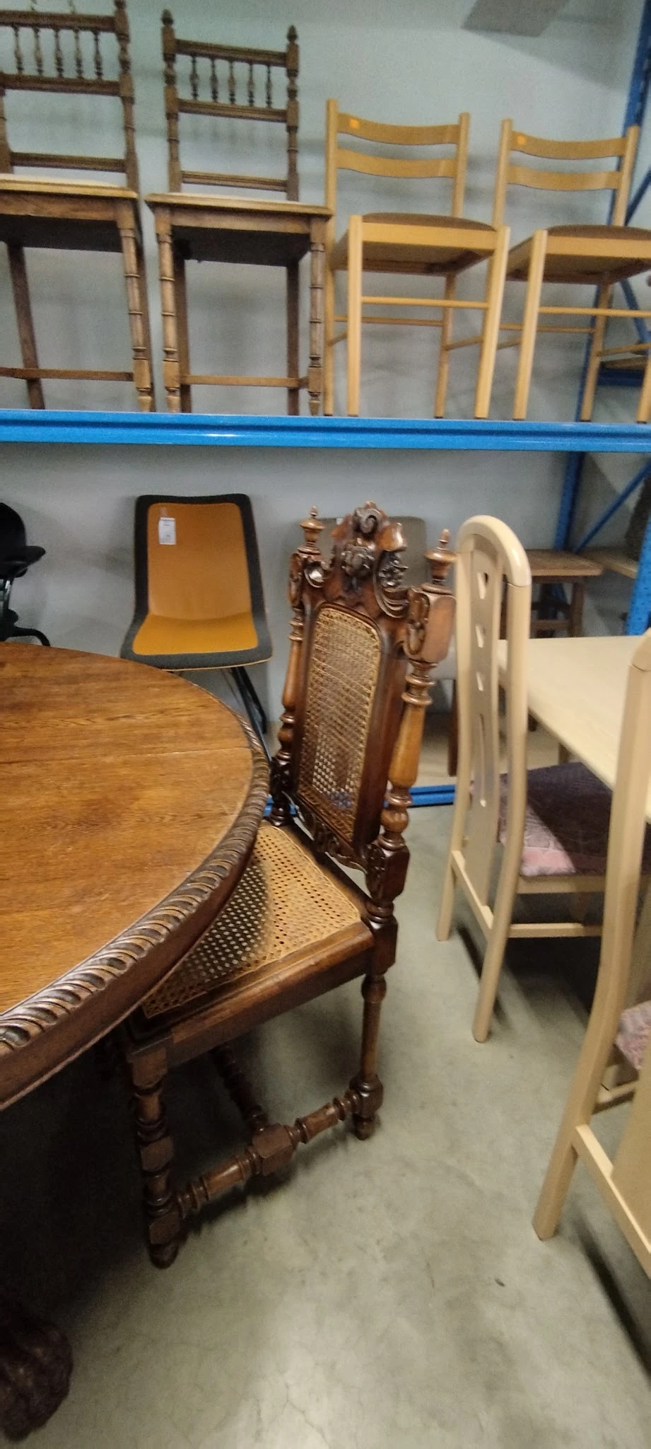 Verschillende meubels in de winkel: houten stoelen met decoratief snijwerk, een gele stoel en witte stoelen