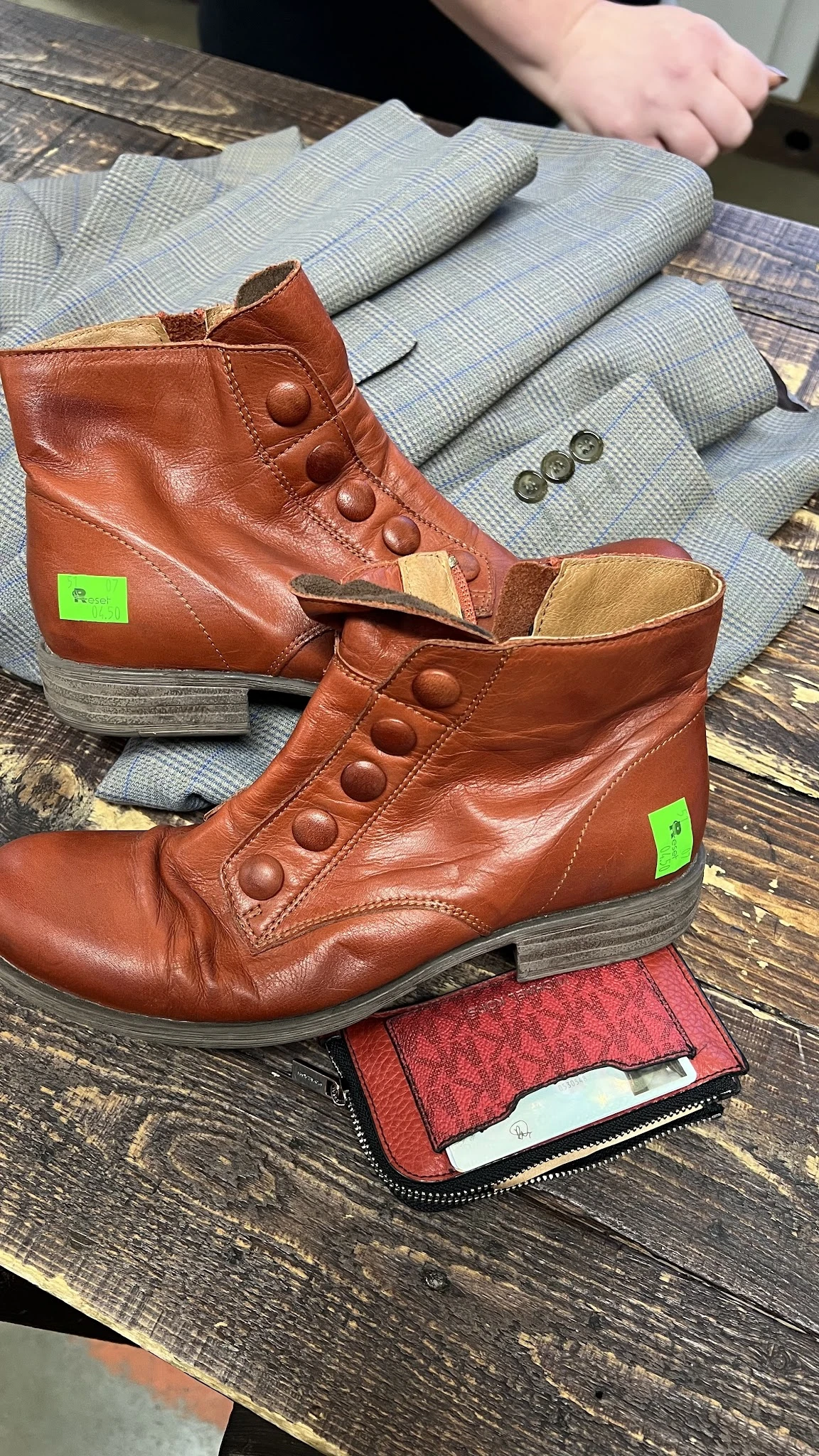 Twee bruine leren laarzen met groene labels en knopen, op textiel en hout