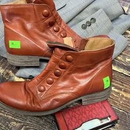 Twee bruine leren laarzen met groene labels en knopen, op textiel en hout
