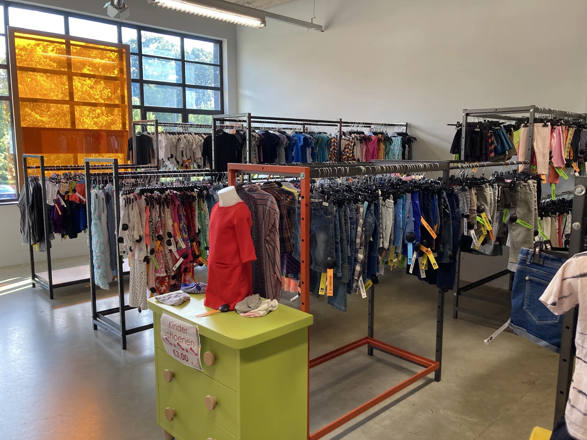 Winkelvloer met kledingrekken en een geel display-podium in een kringloopwinkel