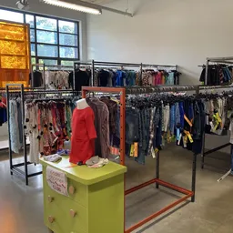 Winkelvloer met kledingrekken en een geel display-podium in een kringloopwinkel
