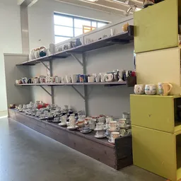 Wandplanken met servies, kannen, mokken en decoratieve items in een kringloopwinkel
