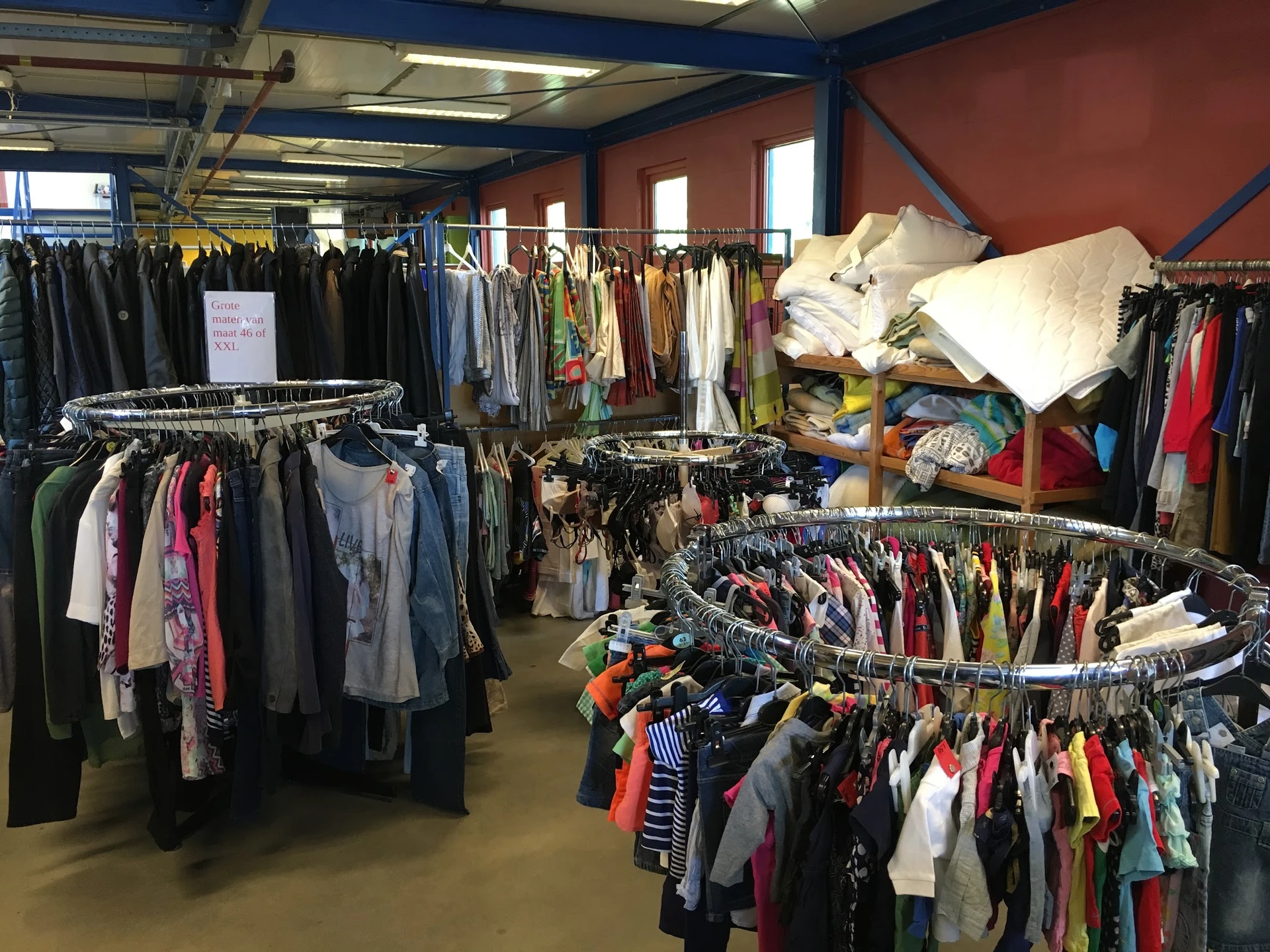 Winkelvloer met meerdere rekken vol tweedehands kleding, daarbovenop stapels witte textiel
