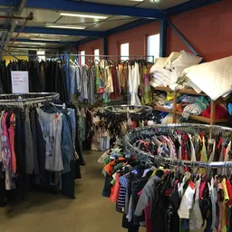 Winkelvloer met meerdere rekken vol tweedehands kleding, daarbovenop stapels witte textiel