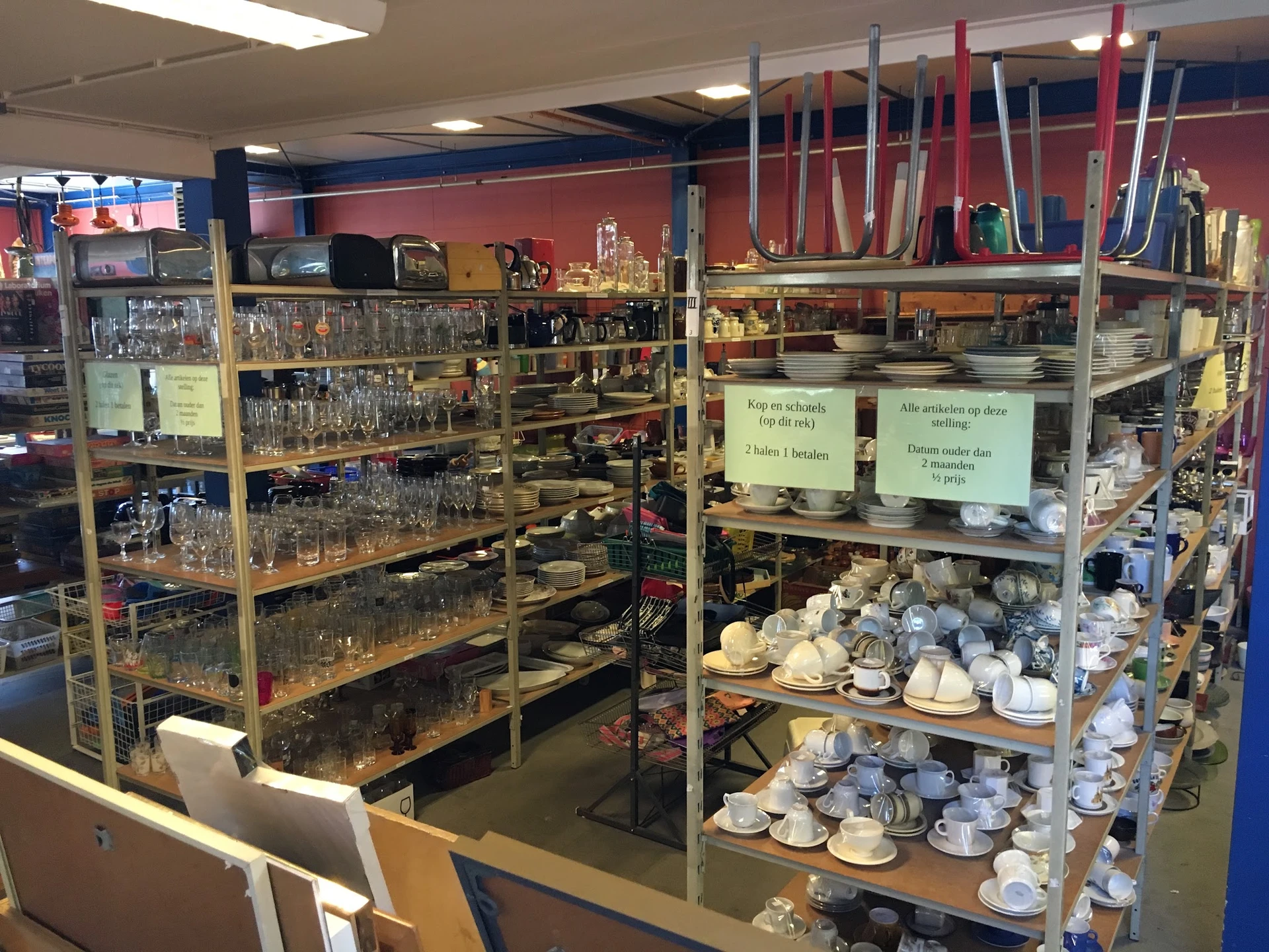 Stellingen met serviesgoed, kopjes, glazen en aardewerk in een kringloopwinkel