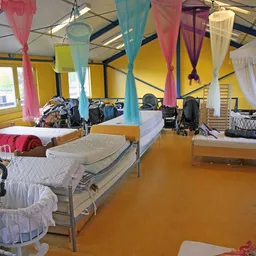 Slaapzaal met meerdere bedden, gekleurde doeken aan het plafond en opgestelde beddenspullen