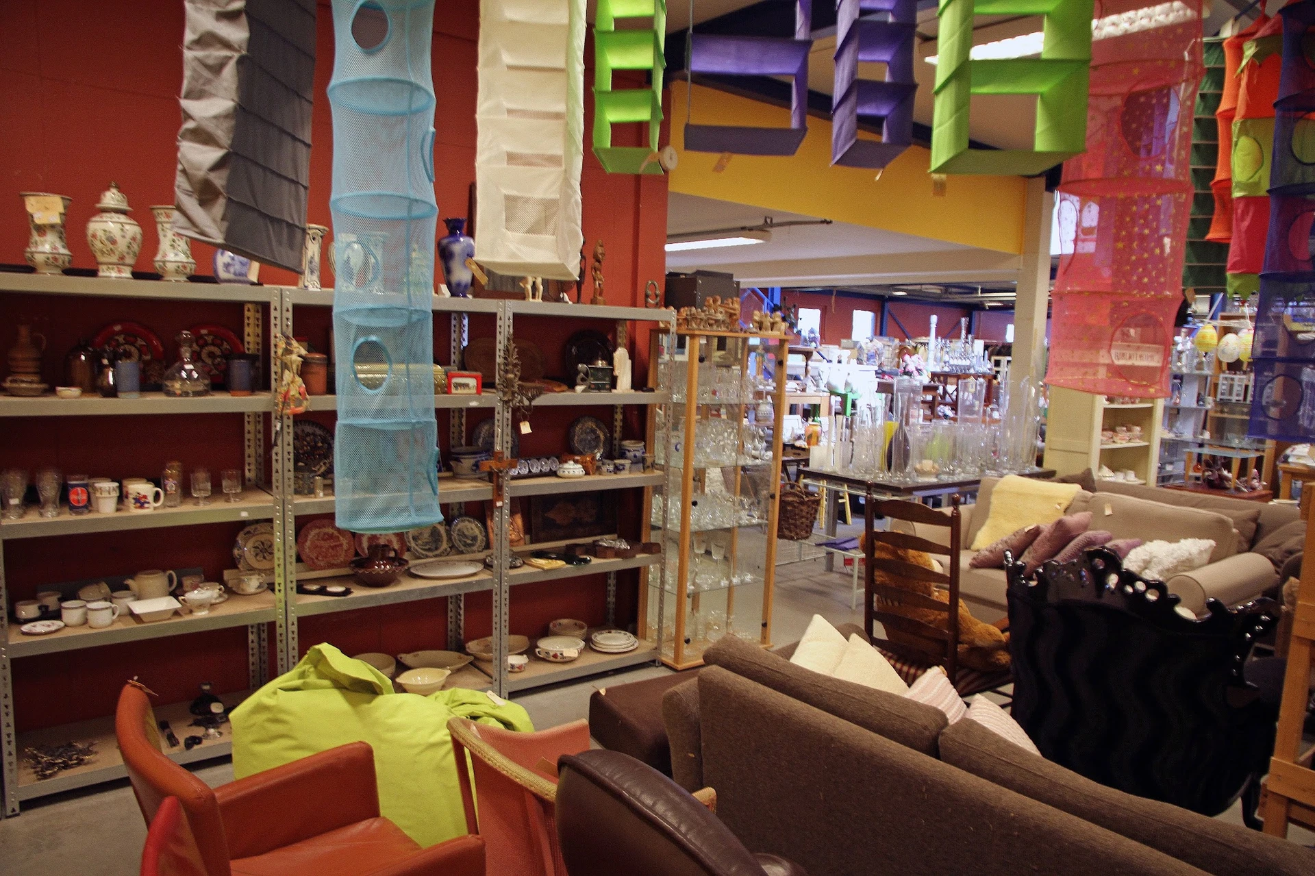 Winkelvloer met stellingen vol huishoudartikelen, decoraties en meubels, oranje stoelen op de voorgrond