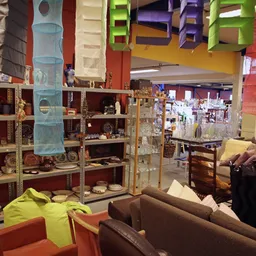 Winkelvloer met stellingen vol huishoudartikelen, decoraties en meubels, oranje stoelen op de voorgrond