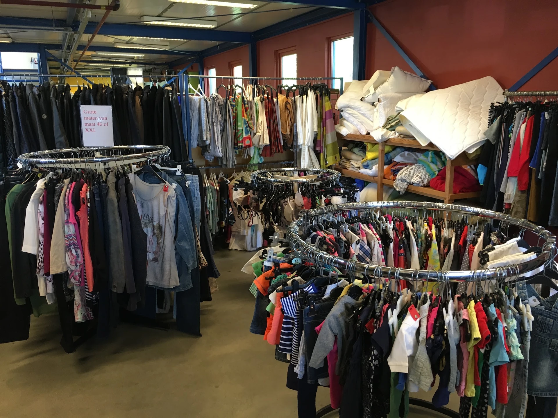 Winkelvloer met meerdere rekken vol tweedehands kleding, verschillende kleuren en stijlen