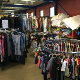 Winkelvloer met meerdere rekken vol tweedehands kleding, verschillende kleuren en stijlen