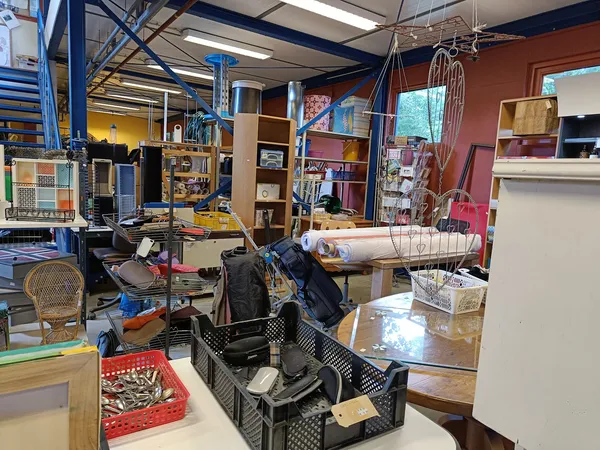 Winkelinterieur met stellingen, diverse spullen, werkstations en opbergtafels vol met tweedehandsartikelen