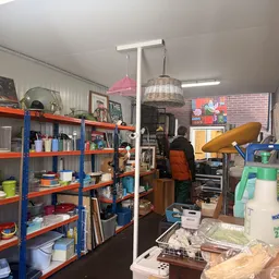 Winkelinterieur met oranje-blauwe stellingen vol spullen, aan de zijkant een werkplek met gereedschap