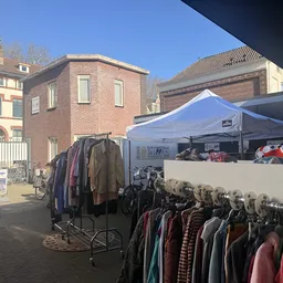 Rekken met tweedehands kleding onder een blauwe marktkraam op een plein