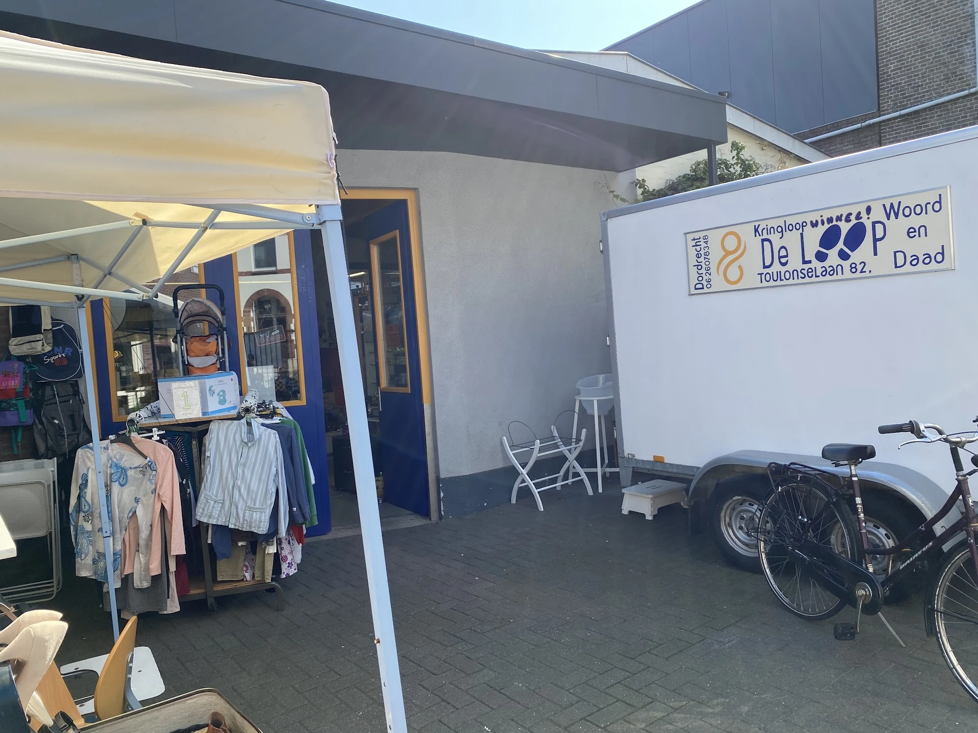 Winkelruimte met kledingrekken, fietsen en een bord met winkellogo tegen de muur