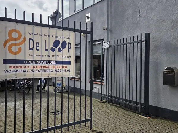 Gevel van kringloopwinkel De Loop met logo, openingstijden en zwart hek ervoor