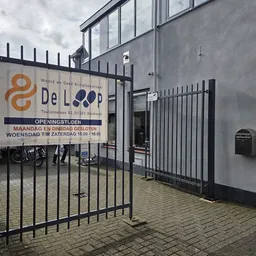 Gevel van kringloopwinkel De Loop met logo, openingstijden en zwart hek ervoor