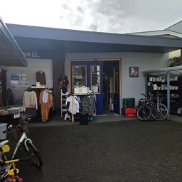 Buitenruimte van kringloopwinkel met rekken tweedehands kleding, fietsen, schappen met spullen en ingangsdeur