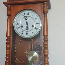 Houten wandklok met wit wijzerplaat en Romeinse cijfers, met slingerwerk eronder
