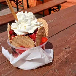 Ijscoupe met wafelkoekje, slagroom en aardbeien op houten terras
