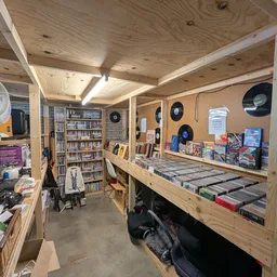Binnenzicht van kringloopwinkel met houten stellingen vol cd's, dvd's, boeken en overige spullen