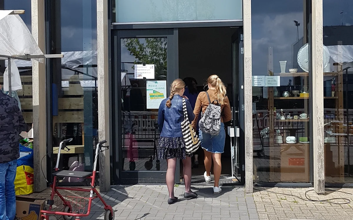 Ingang van kringloopwinkel de Mors met twee vrouwen in de deuropening, winkelnaam zichtbaar boven