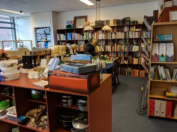 Winkelvloer met boekenkasten, oranje toonbank met keukengerei en diverse tweedehands spullen