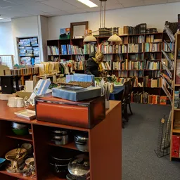 Winkelvloer met boekenkasten, oranje toonbank met keukengerei en diverse tweedehands spullen