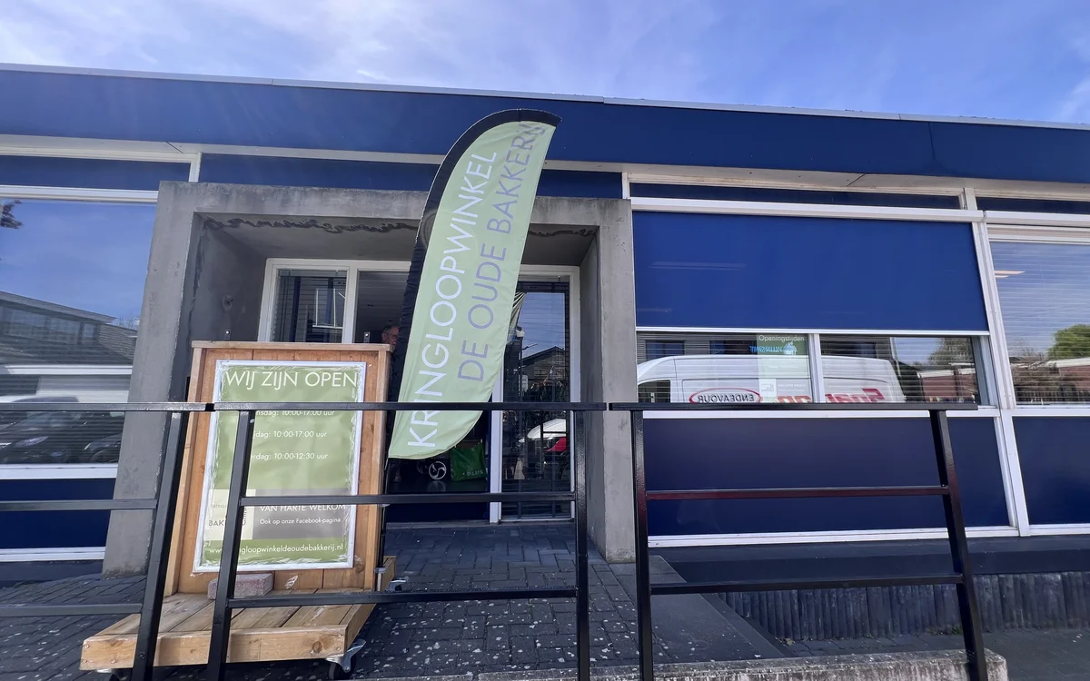 Gevel van kringloopwinkel met blauwe puien, ingang met trap en openingsbord