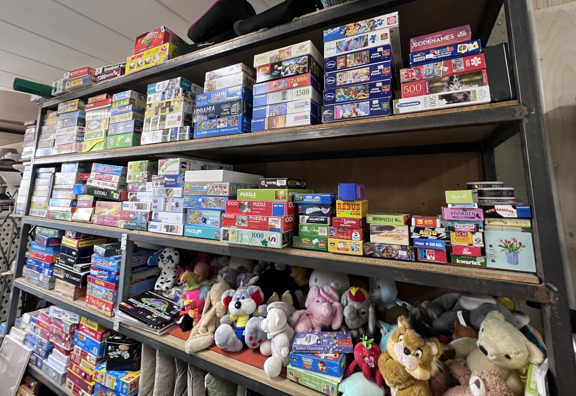 Stellingen met bordspellen, puzzels en knuffelbeesten in een kringloopwinkel