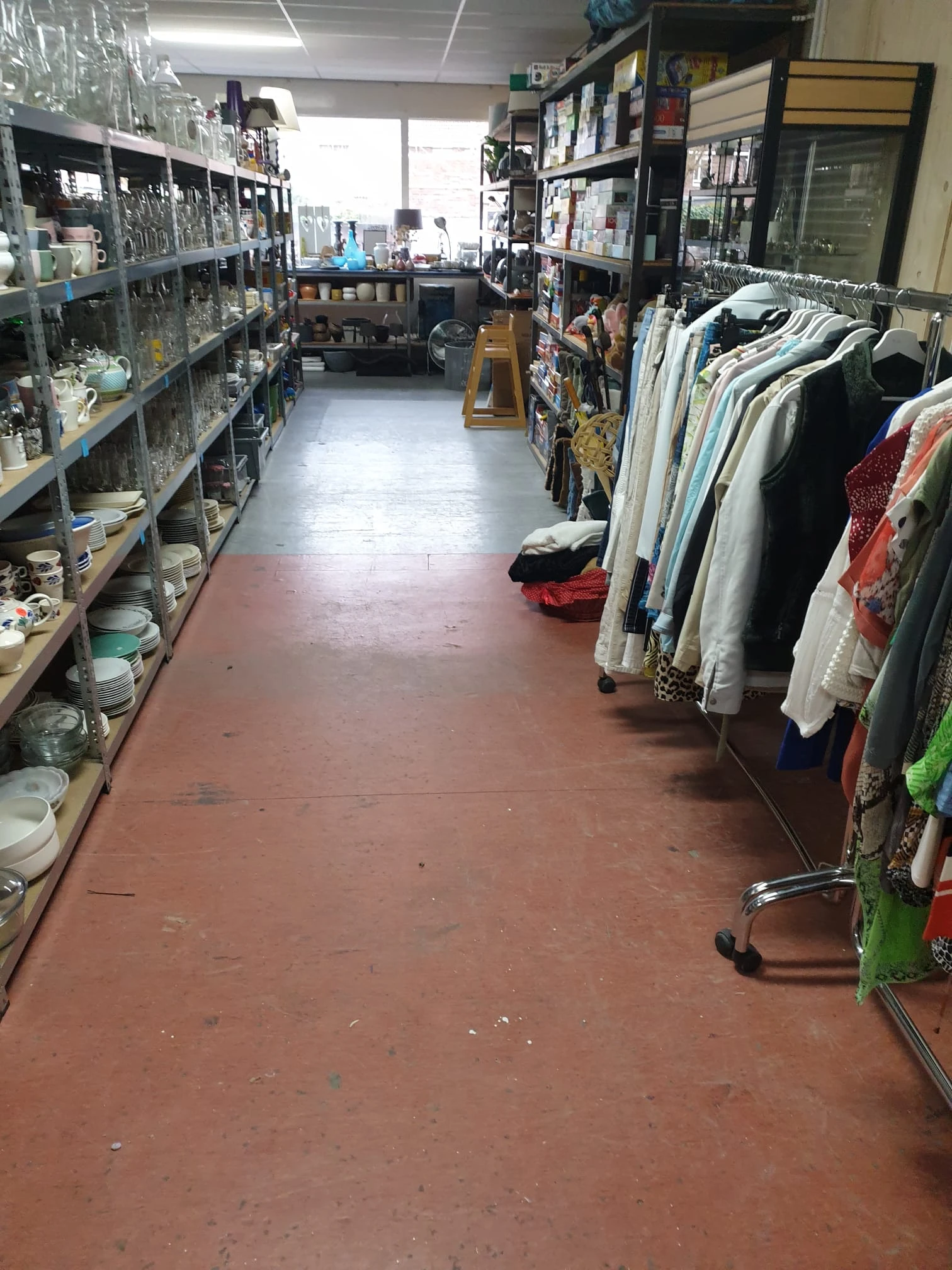 Winkelpad met aan linkerzijde schappen met huishoudartikelen en aan rechterzijde rekken met kleding