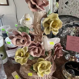 Decoratieve kunstbloemen in roze en geel op een houten tak, met witte vogel en groen blad