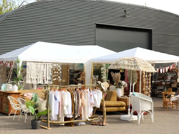 Buitenopstelling met kledingrekken, meubels en decoratie onder witte en rieten parasols