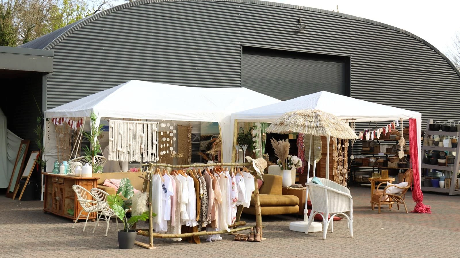 Buitenopstelling met kledingrekken, meubels en decoratie onder witte en rieten parasols