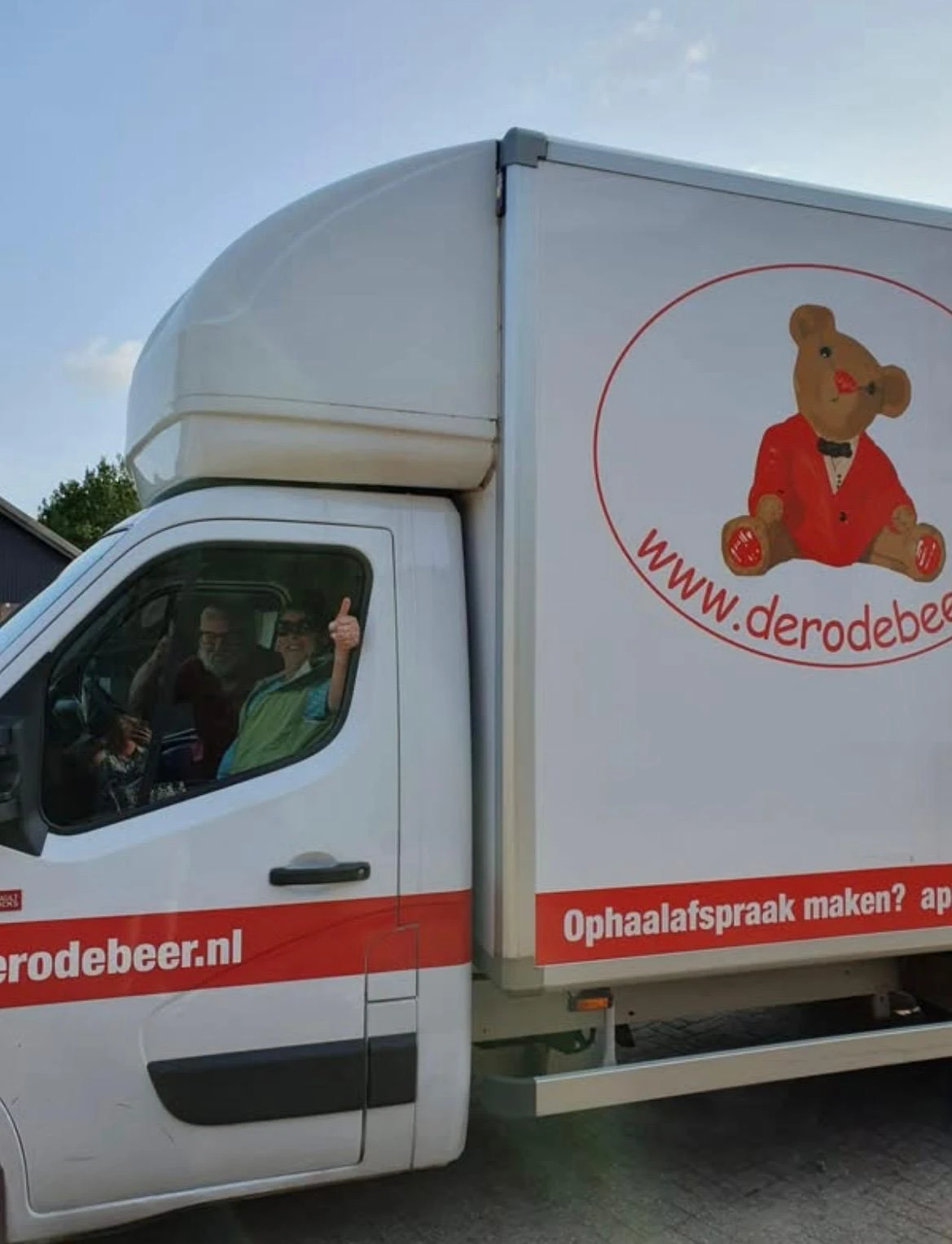 Bedrijfsbus van kringloopwinkel De Rode Beer met bestuurder en passagier zichtbaar in de cabine