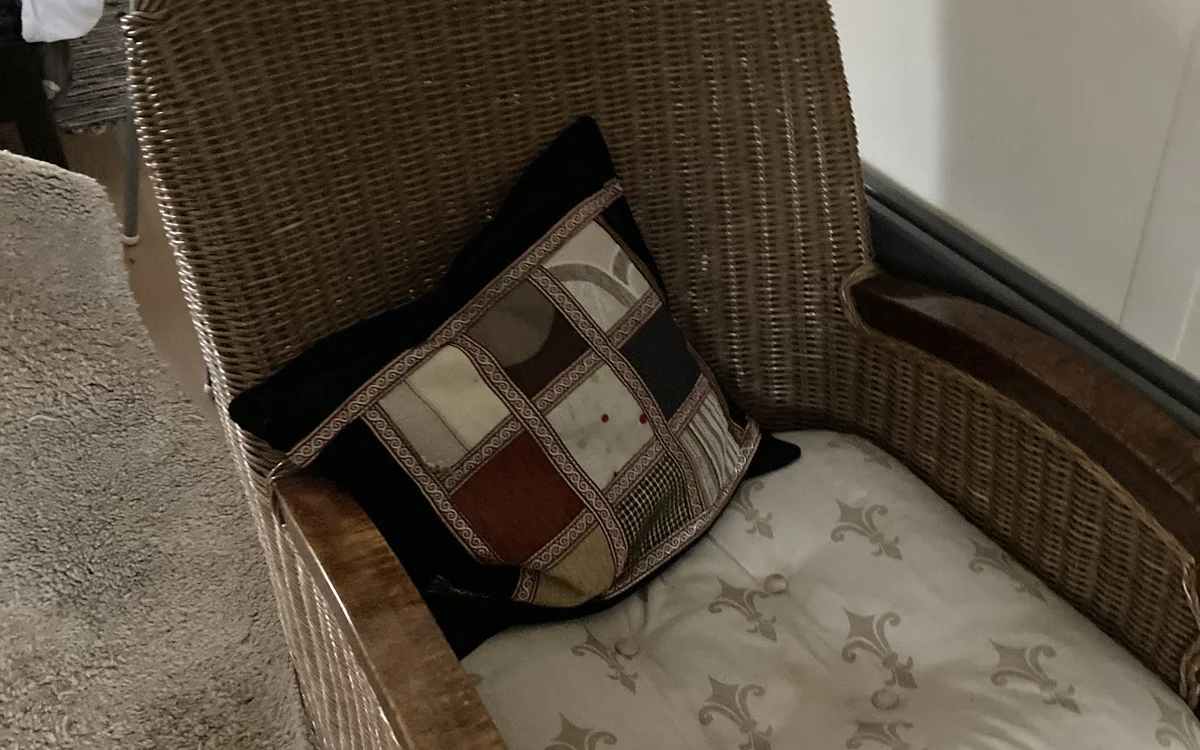 Rieten stoel met gekleurde patchwork kussen en gestreepte rug in tweedehands winkel