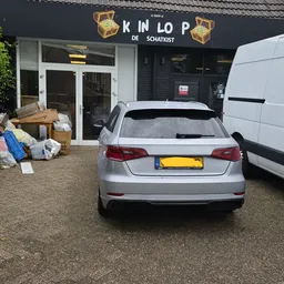 Grijze auto geparkeerd voor de winkel met dozen en spullen op het trottoir