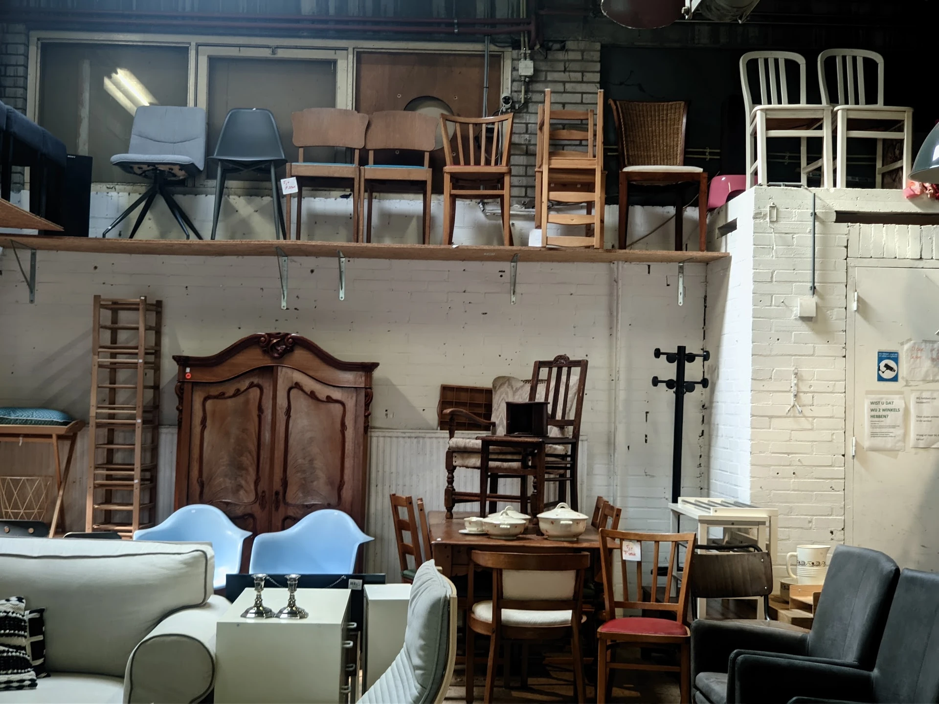 Diverse meubels en stoelen uitgestald in een kringloopwinkel, waaronder houten kasten, stoelen en een grijze bank