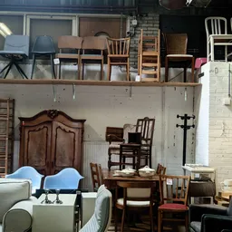 Diverse meubels en stoelen uitgestald in een kringloopwinkel, waaronder houten kasten, stoelen en een grijze bank